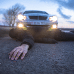 An individual is sprawled on the ground next to a vehicle, suggesting a possible accident.