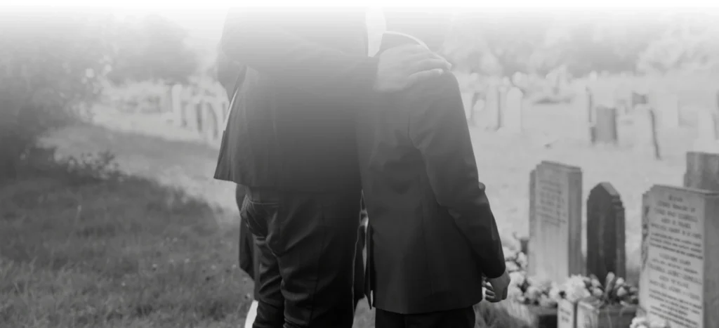 Two people consoling each other in a graveyard with tombstones in the background.