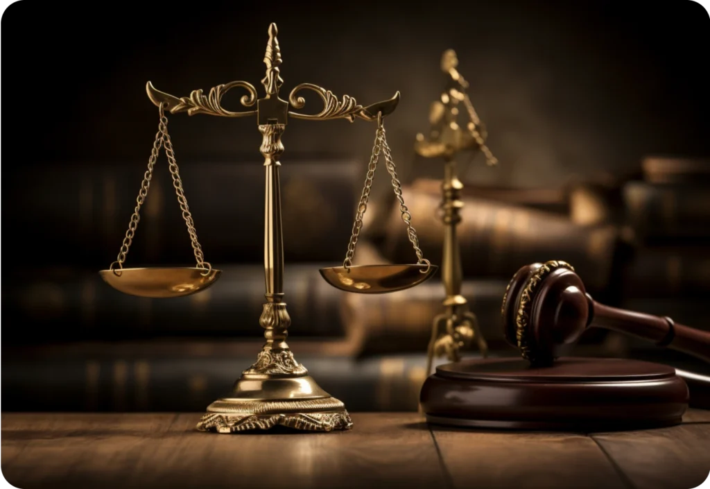 A close-up of ornate golden scales of justice displayed on a wooden table. A judge’s gavel and blurred law books sit in the background, all lit with warm, dramatic lighting.