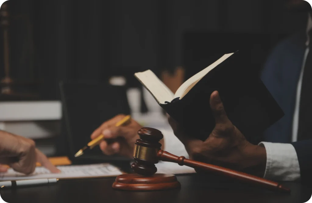Attorney with an open book and gavel, discussing with someone at a desk.