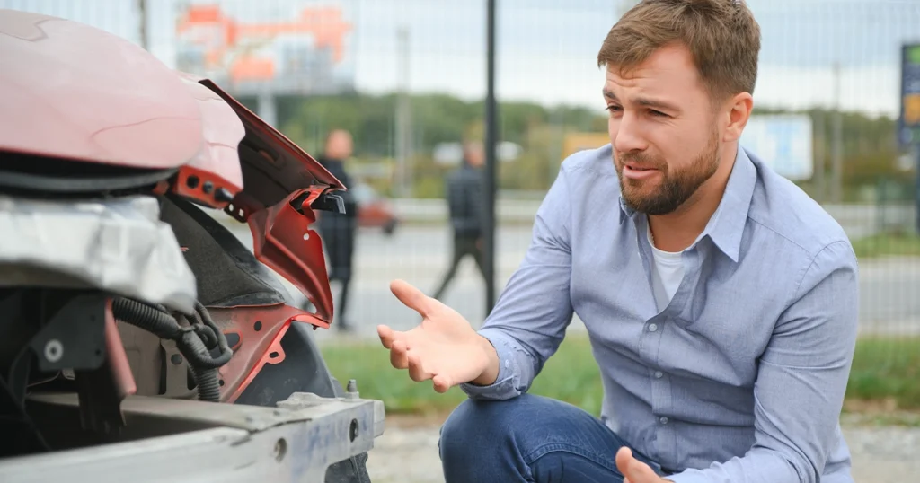 Driver kneeling beside crashed car, unsure what to do.
