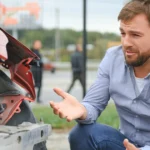 Driver kneeling beside crashed car, unsure what to do.