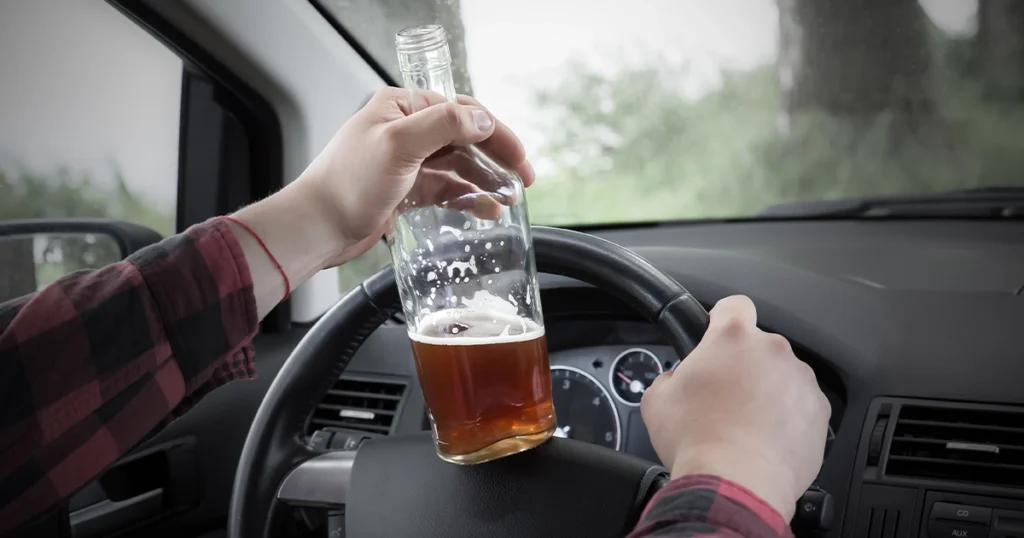 Hand holding a beer bottle while driving a car.