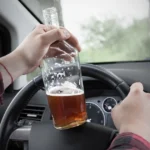 Hand holding a beer bottle while driving a car.