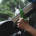 Driver holding an open beer bottle behind the wheel.