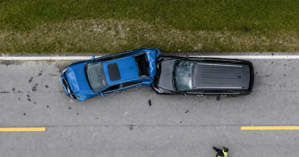 Aerial view of a blue car and black SUV after a crash on a road, with a responder standing nearby.