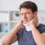 Man wearing a neck brace, holding his neck in pain in a bright clinic setting.