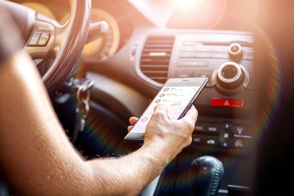 Close-up of a person using a mobile phone while sitting in the driver's seat of a vehicle.