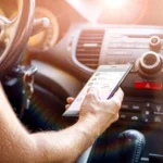 Close-up of a person using a mobile phone while sitting in the driver's seat of a vehicle.