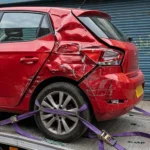 A damaged red car secured with purple straps on a flatbed tow truck.