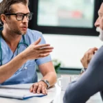 Male doctor in scrubs explaining medical details to senior patient.