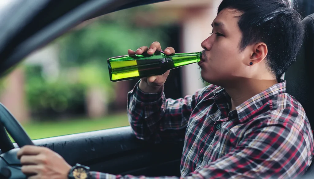 Man drinking bottled beer while sitting behind car steering wheel