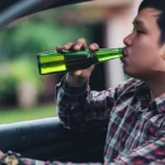 Man drinking bottled beer while sitting behind car steering wheel